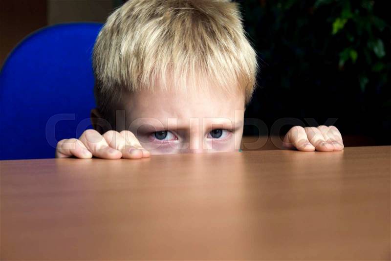 Sad upset unhappy boy kid hiding under the table, stock photo
