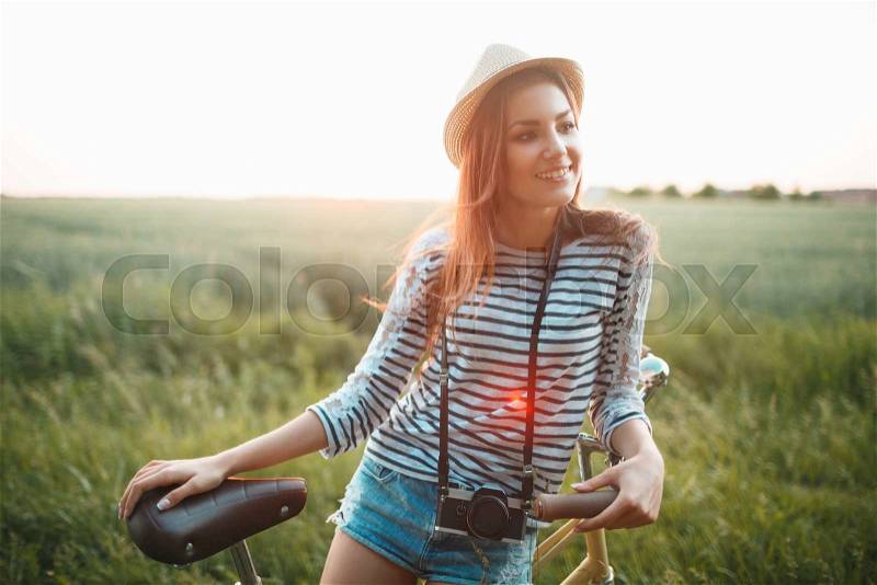 Lovely young woman stands in a field with her bicycle. Lifestyle concept, stock photo