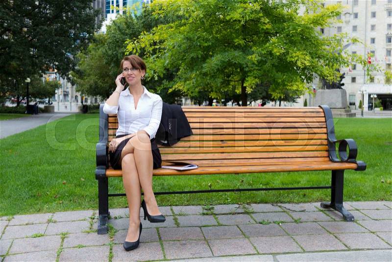 Business woman on park bench talks on phone, stock photo