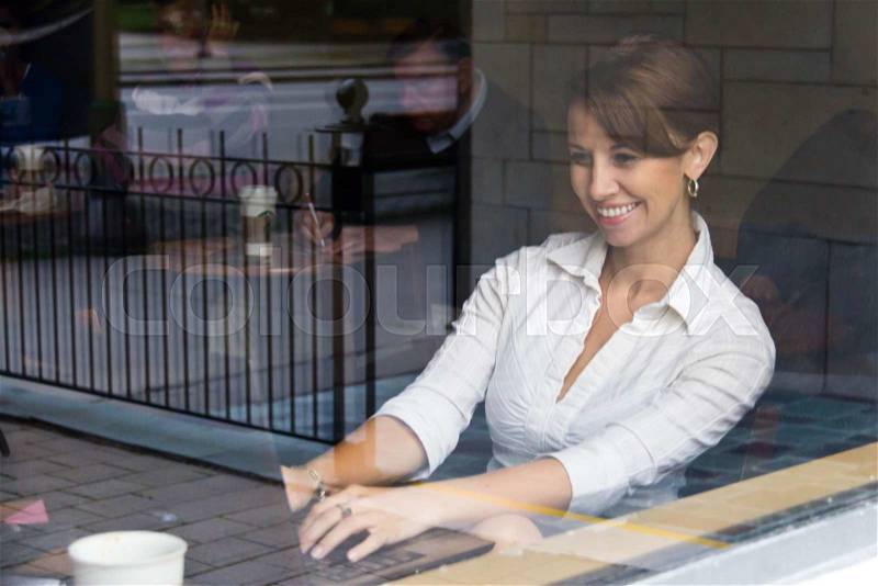 Woman inside coffee shop working on laptop, stock photo