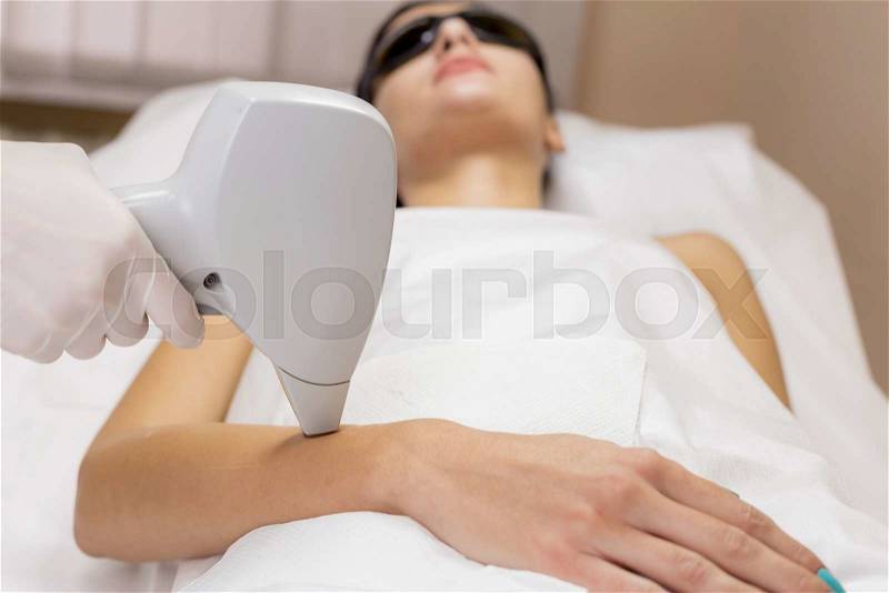 Laser hair removal on client hand in beauty cosmetic salon. Patient lie on couch in black glasses. Intentional shallow depth of field, stock photo