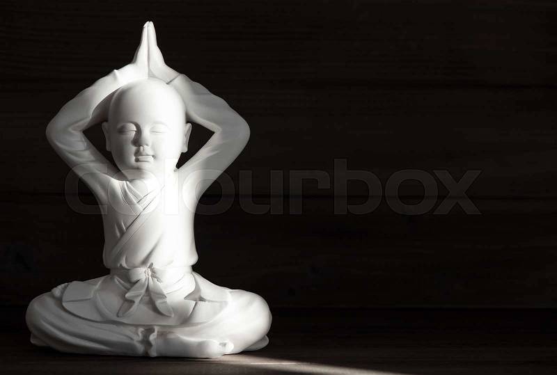 Sitting buddha. White monk statue on dark background. Meditation and relaxing concept, stock photo