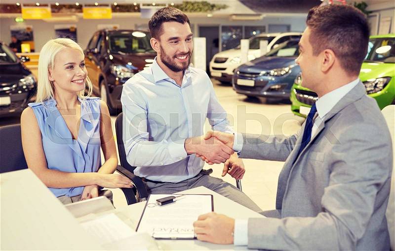 Auto business, car sale, and people concept - happy couple with dealer shaking hands in auto show or salon, stock photo