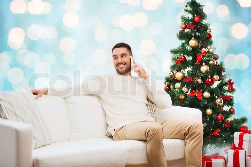 Christmas, technology, people and holidays concept - smiling man calling on smartphone over blue holidays lights background, stock photo