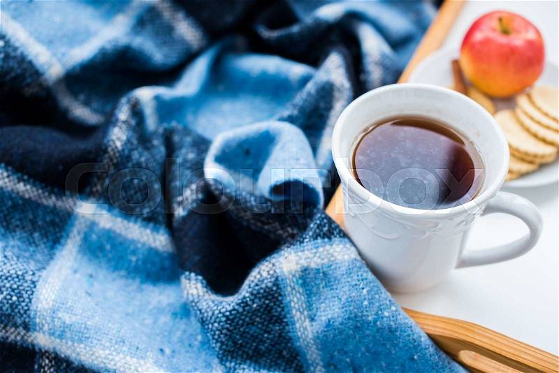 Cozy breakfast: cup of hot tea, apple, cookies and a blue checkered woolen plaid. Cozy winter home arrangement, stock photo