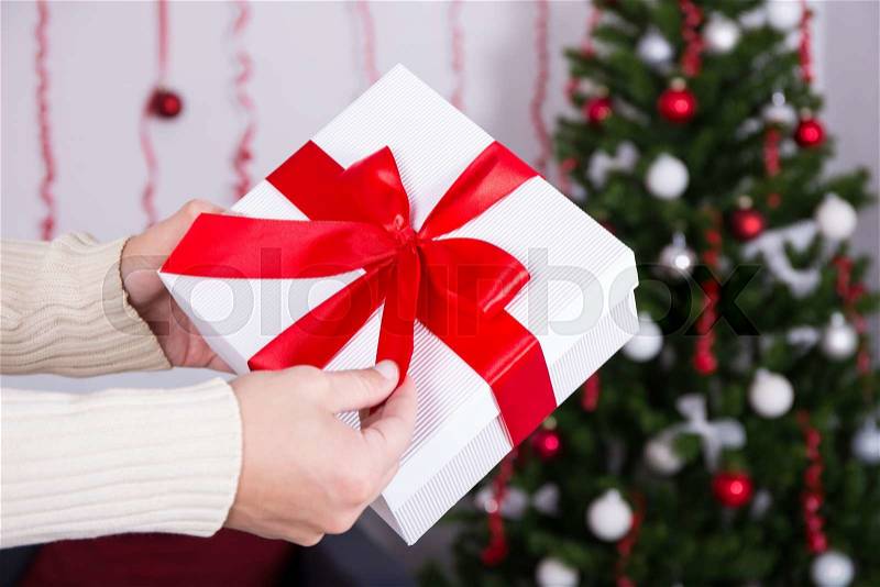 Christmas concept - gift box in male hand over Christmas interior, stock photo