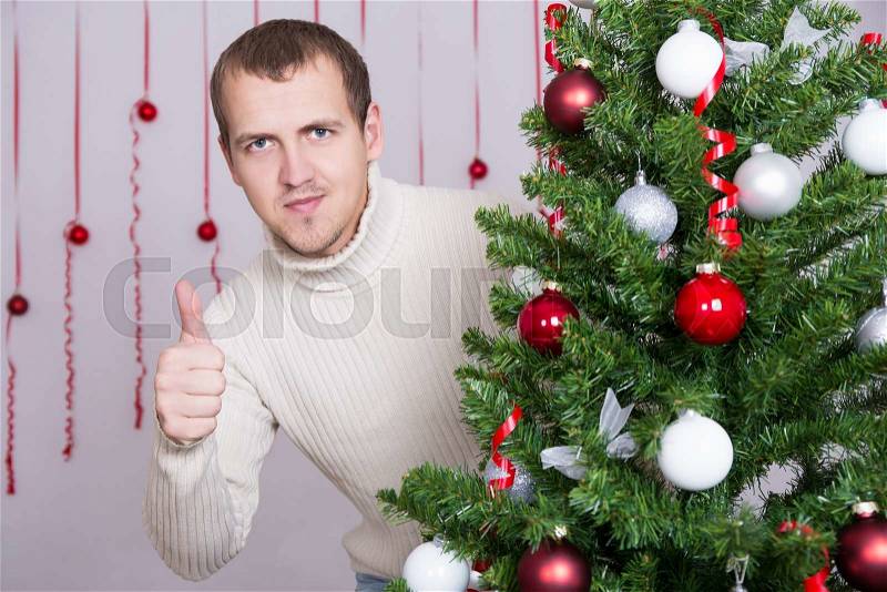 Portrait of happy handsome man thumbs up and decorated Christmas tree, stock photo