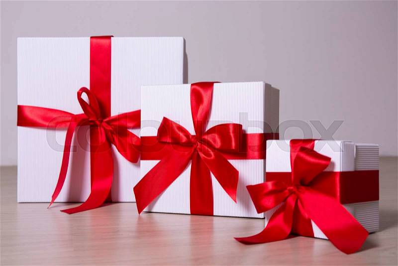 White gift boxes with red ribbon and bows on wooden background, stock photo
