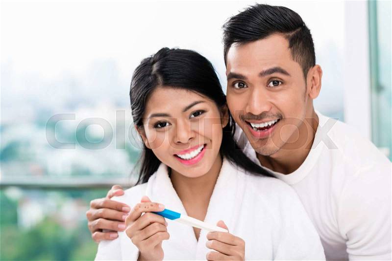 Asian woman surprising her husband with positive pregnancy test, he seems reasonably pleased, stock photo