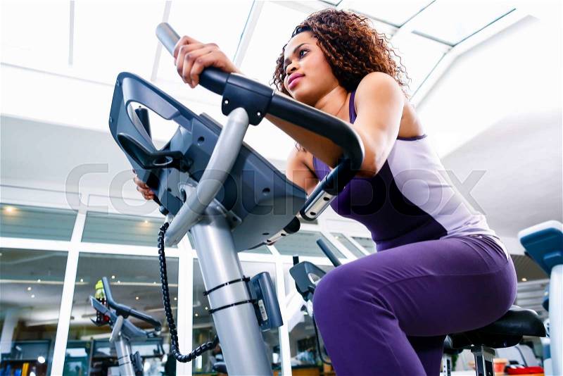 African woman in gym spinning on fitness bike, stock photo