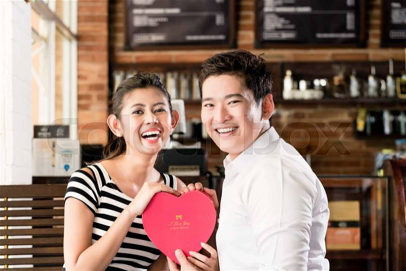 Asian couple, woman and man, having date in coffee shop with red heart, flirting or celebrating anniversary, stock photo