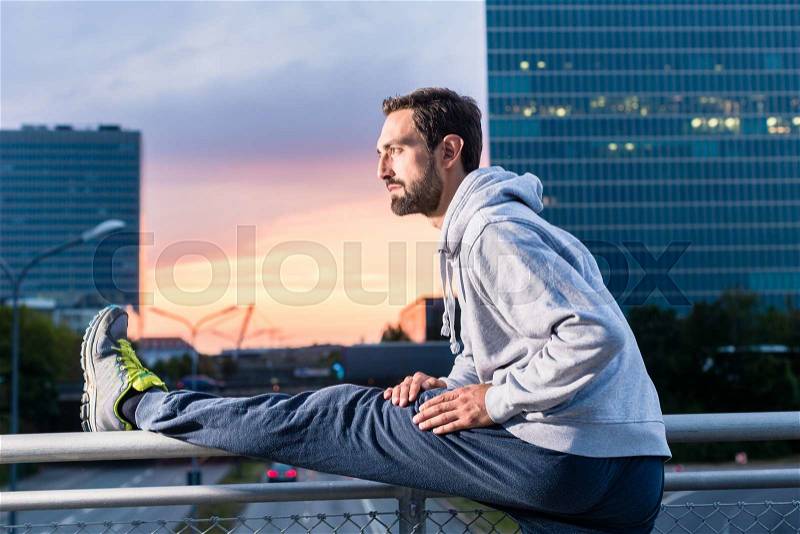 Runner stretching in front of office building at sunset, stock photo