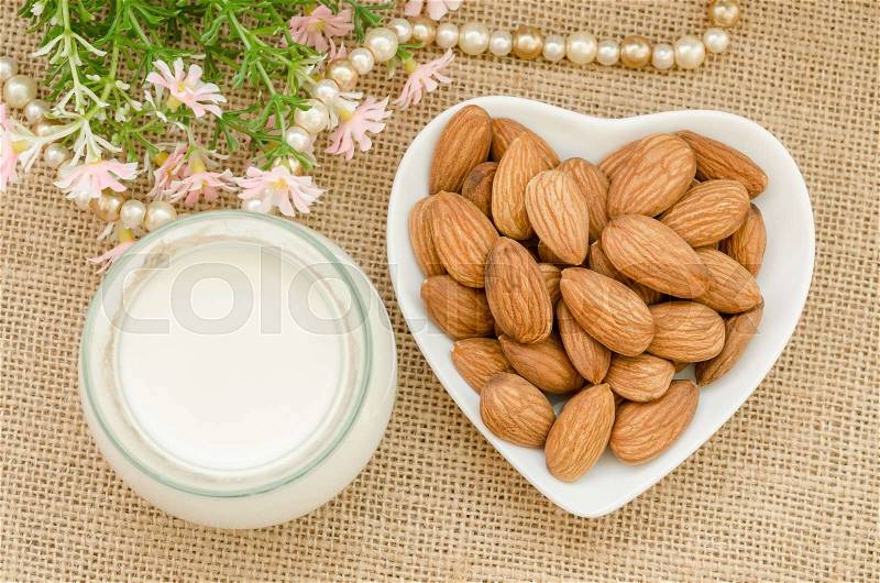 Almond milk with almond on a white bowl cup with flower on sack background, stock photo