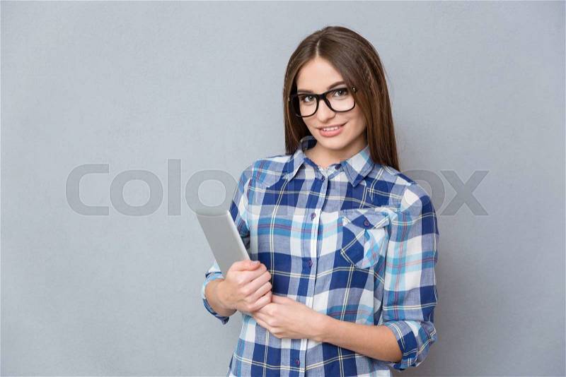Portrait of cute smiling pretty young woman in checkered shirt and glasses holding tablet, stock photo