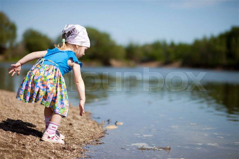 Little girl in blue dress throwing stones into a lake, stock photo