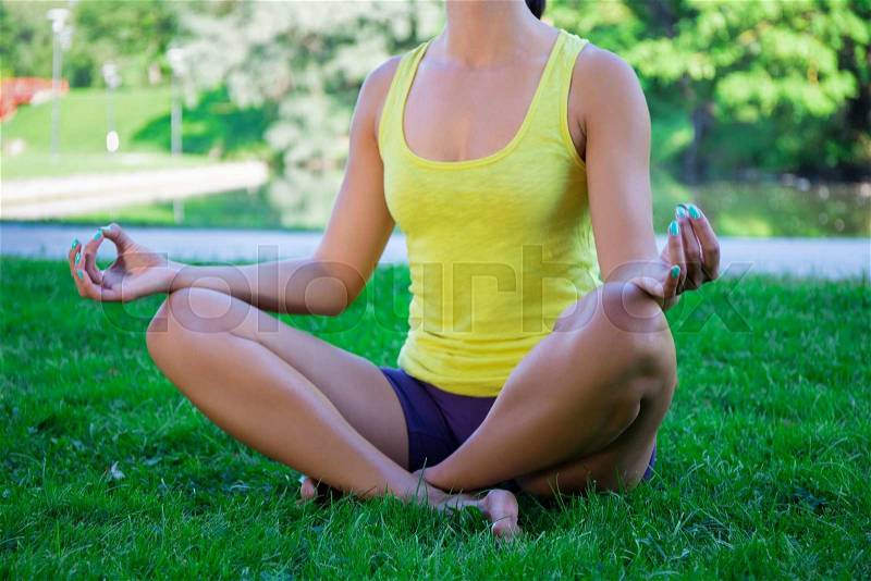 Yoga concept - close up of slim woman sitting in lotus pose in park, stock photo