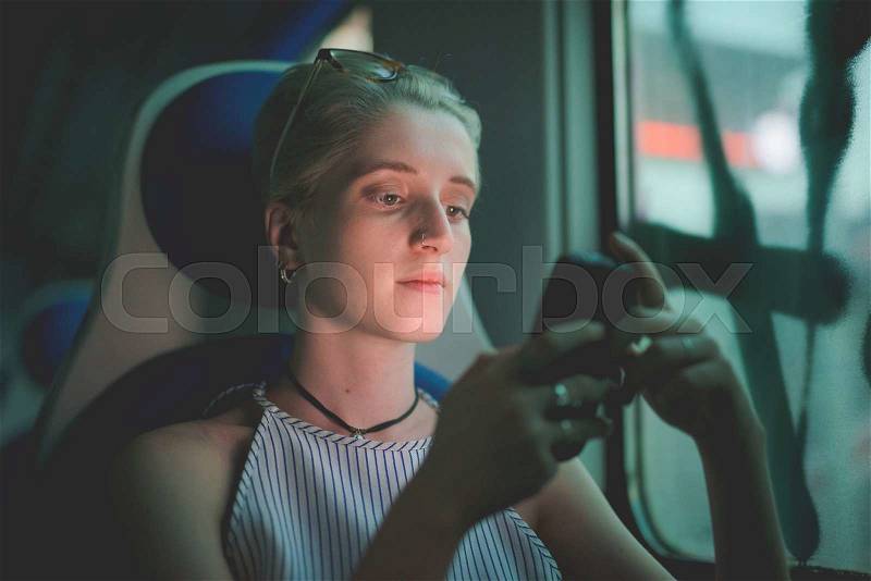 Half length of a young handsome caucasian blonde italian designer sitting in a train, holding a smartphone, looking down the screen, pensive- technology, social network, communication concept, stock photo