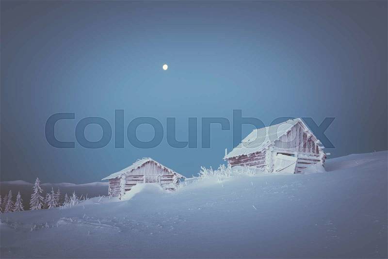 Wooden house in the mountain village. Morning twilight. Winter landscape with snow drifts. The full moon in the clear sky. Color toning. Low contrast, stock photo