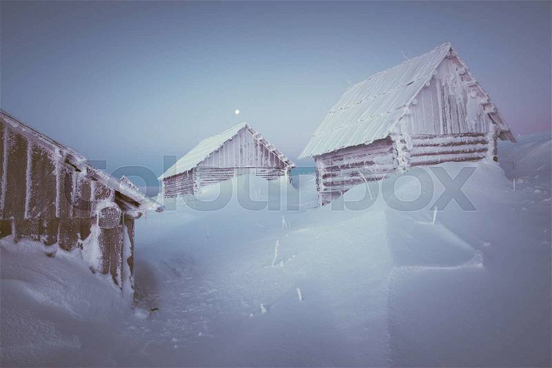 Old wooden house in a mountain village. Morning twilight. Winter landscape with snow drifts. Color toning. Low contrast, stock photo