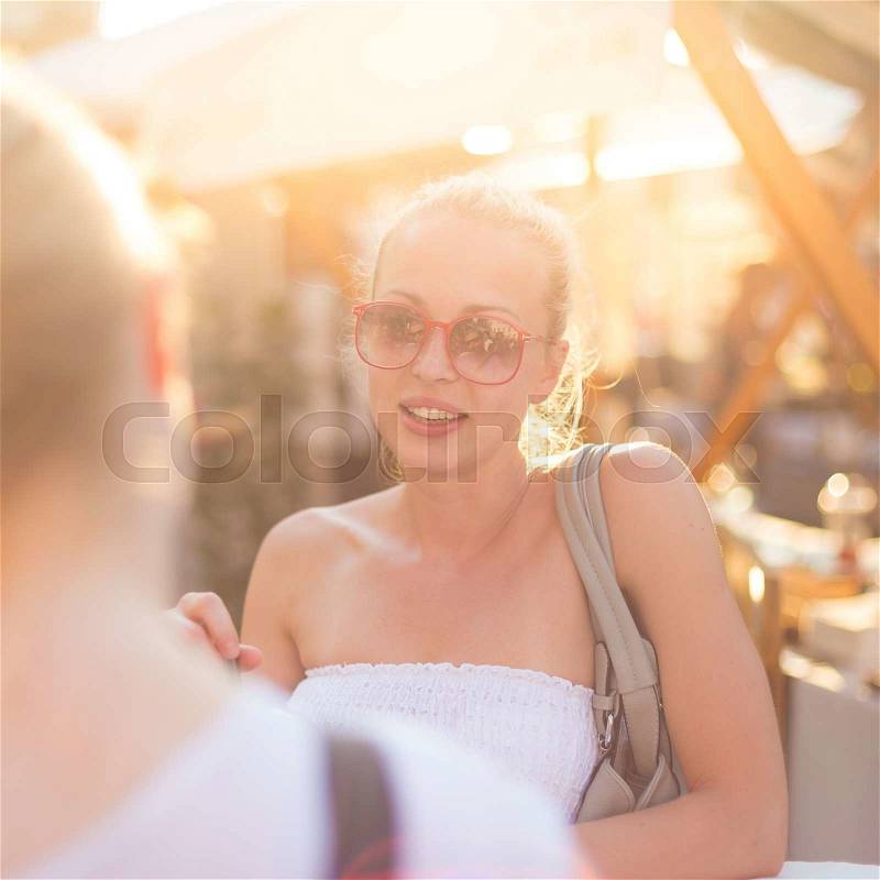 It is nice to see you. It has been a while. Two happy young female friends enjoying a conversation on urban food market at random after work encounter. Pleasant free time socializing, stock photo