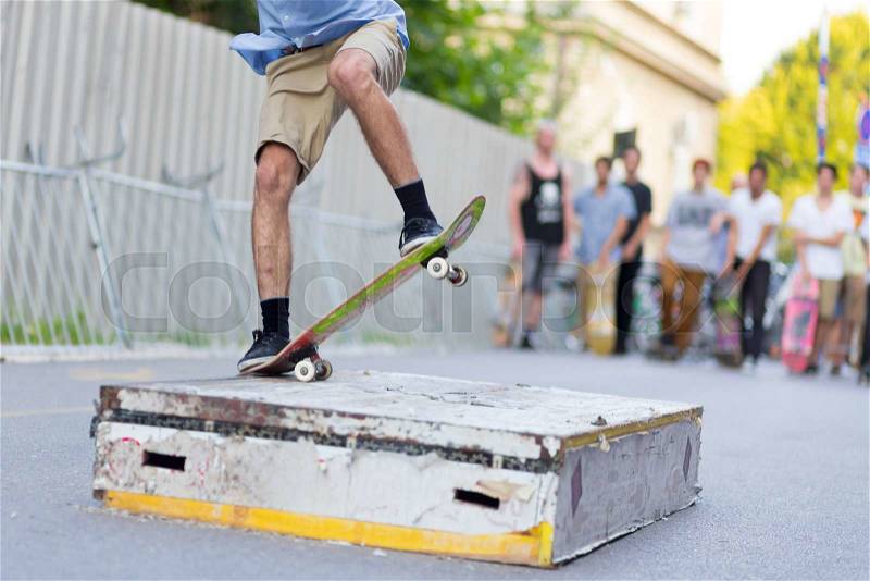 Young skateboarder skateboarding on the street. Skateboarding legs doing slide trick on object. Group of friends cheering in the background, stock photo