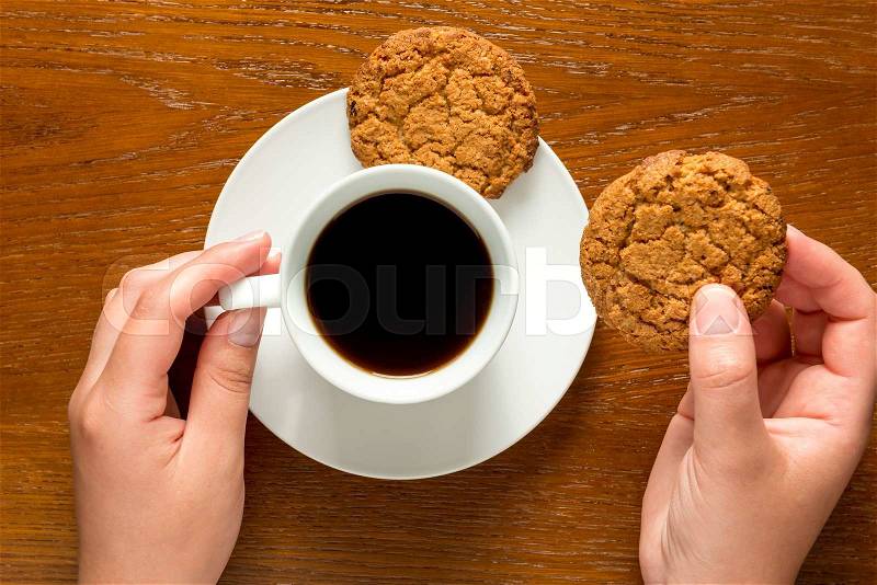 Hands holding a cup of coffee and cookies top view, stock photo