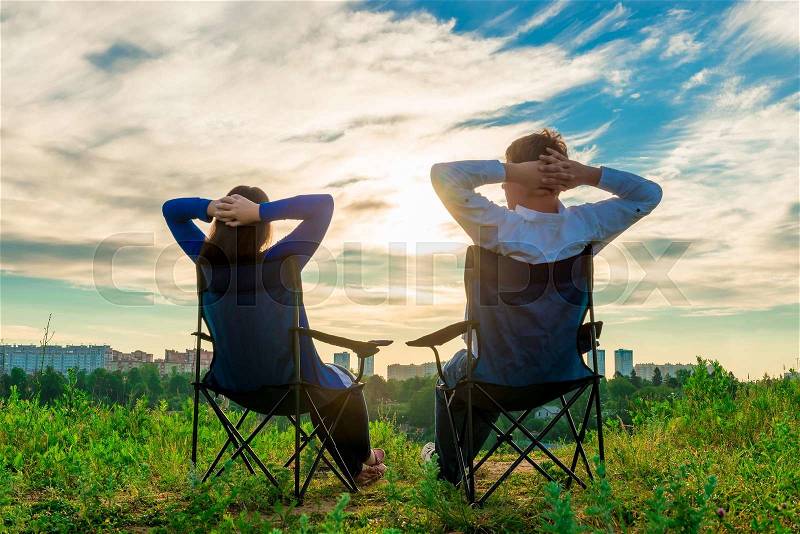 Man and woman sitting in chairs and admire the sunrise over the city, stock photo