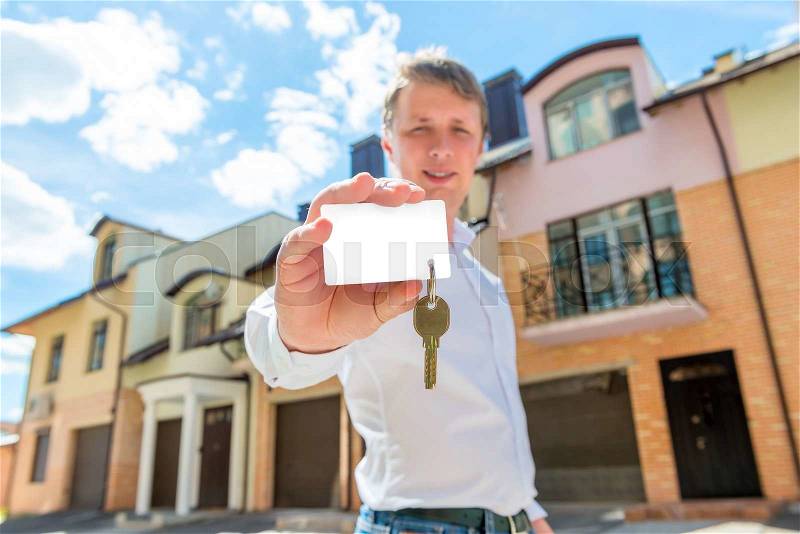 Man stands near the house and shows the key to the apartment, stock photo