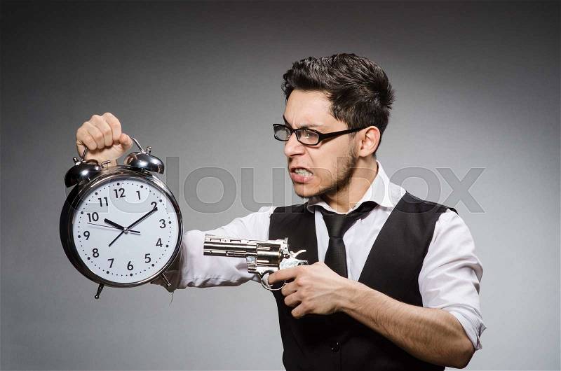 The employee holding alarm clock and handgun against gray, stock photo
