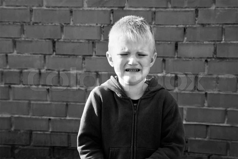 Crying sad upset child (caucasian boy, kid) near red brick wall, stock photo
