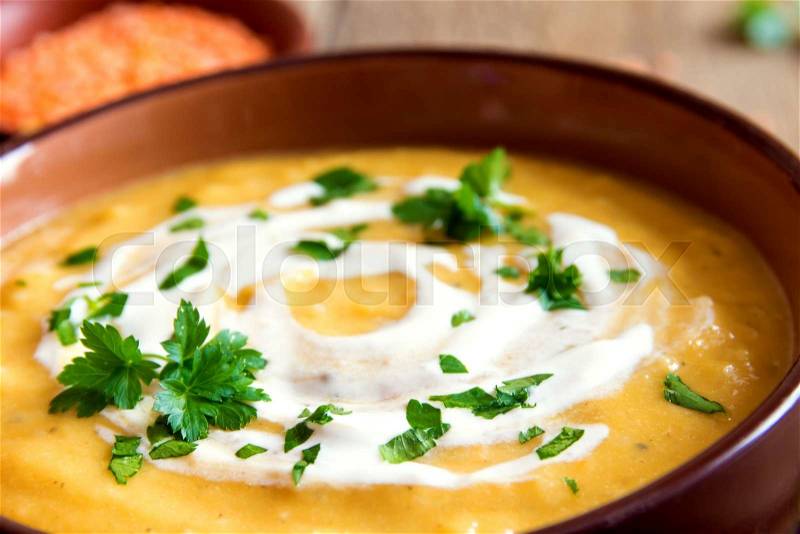 Lentil cream soup with cream cheese and parsley in bowl over rustic wooden background, stock photo