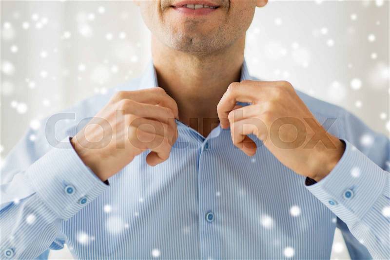 People, business, fashion and clothing concept - close up of smiling man dressing up and adjusting shirt collar at home over snow effect, stock photo