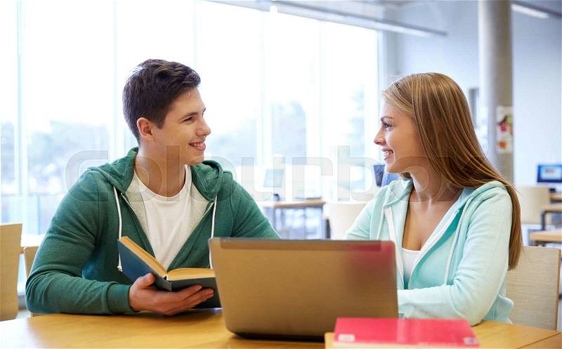 People, education, technology and school concept - happy students with laptop computer and books in library, stock photo