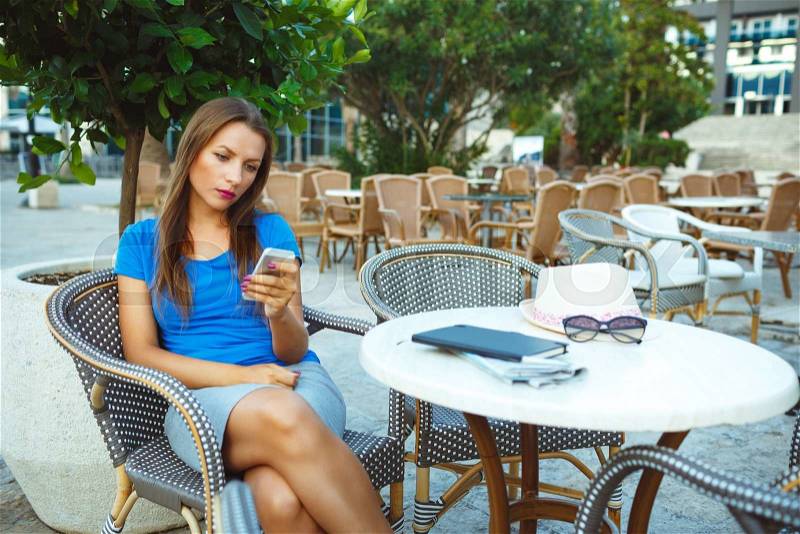 Young pretty woman relaxing in the outdoor cafe and using smartphone - lifestyle concept, stock photo