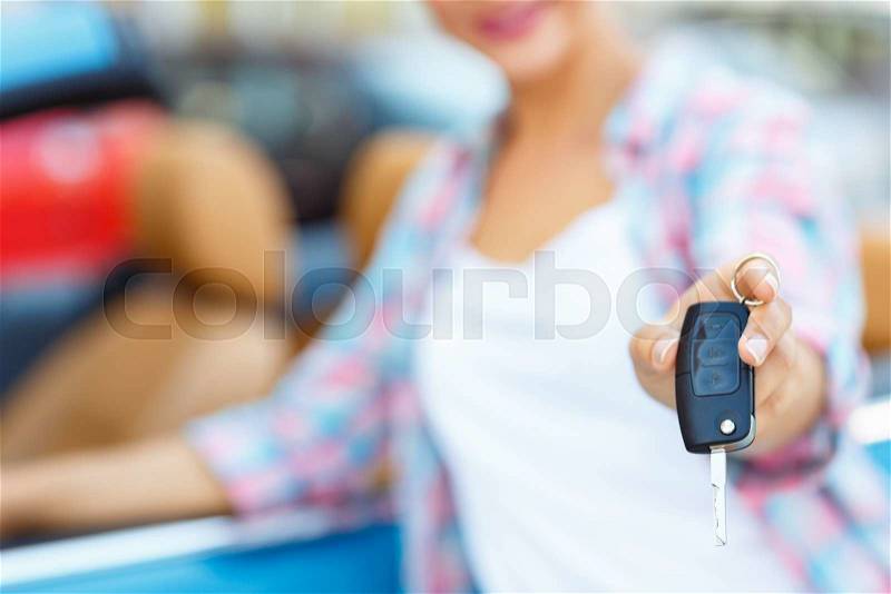 Young woman standing near a convertible with keys in hand - concept of buying a used car or a rental car, stock photo