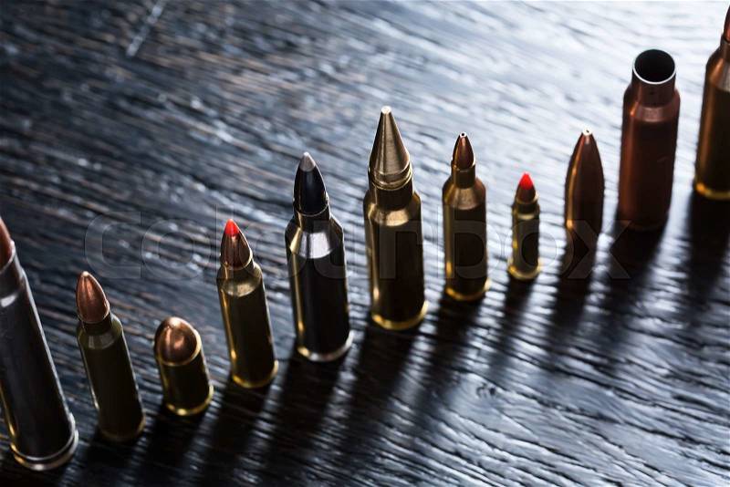 Number of large-caliber ammunition of different caliber in one line on a dark textural wooden background. Studio shot, stock photo