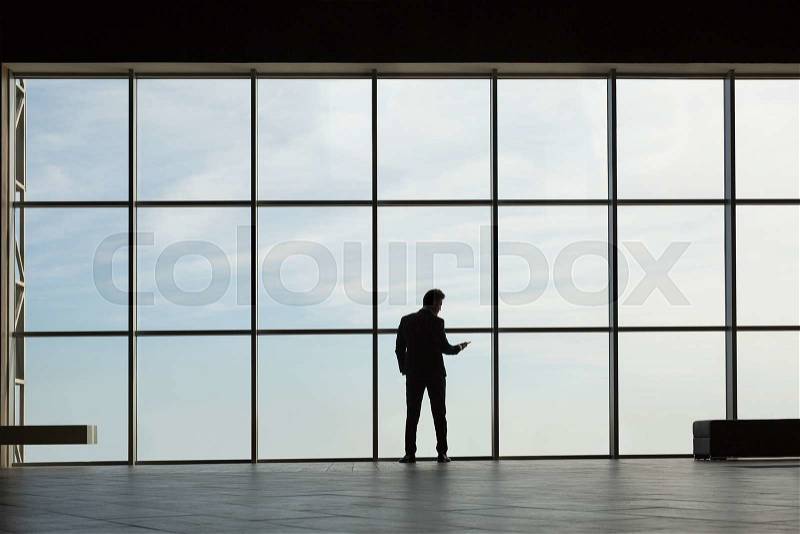 Stylish business man in the background of a large window in the floor. Model talking on the phone, stock photo