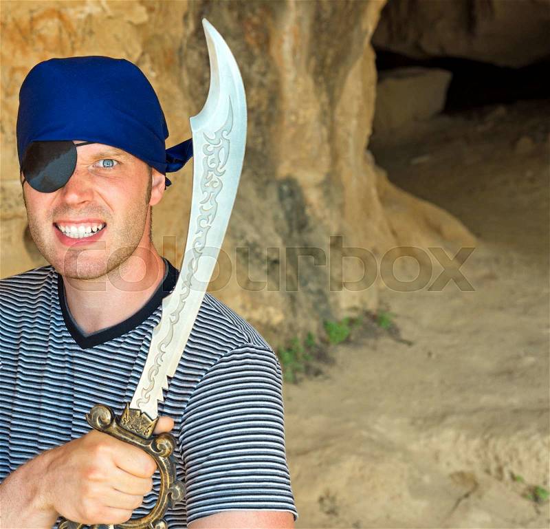 Angry male pirate with sword near the cave entrance. Place for your text, stock photo