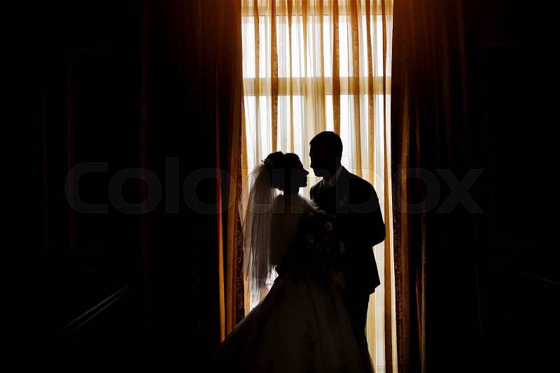 Silhouette of a bride and groom on the background of a window with curtains, stock photo