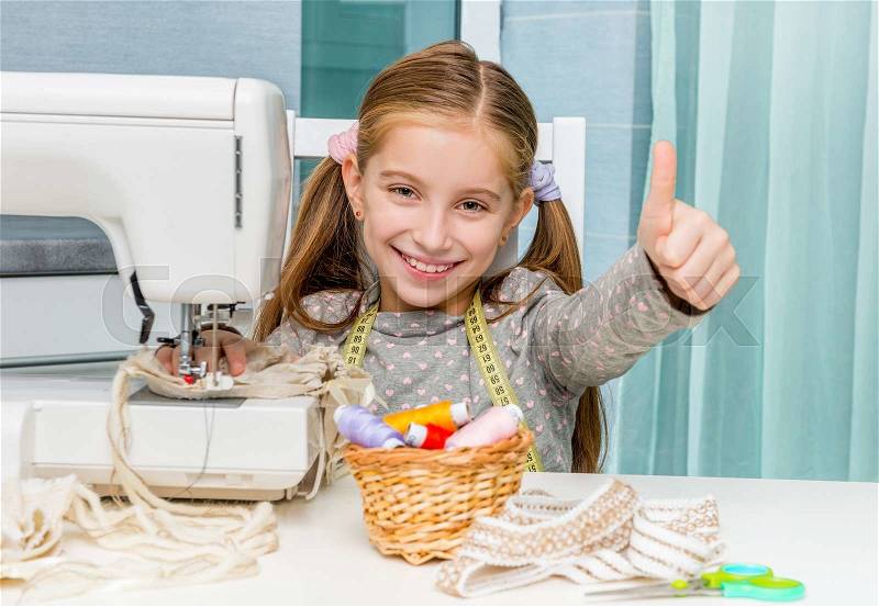 Smiling little girl at the table with sewing machine show thumb, stock photo
