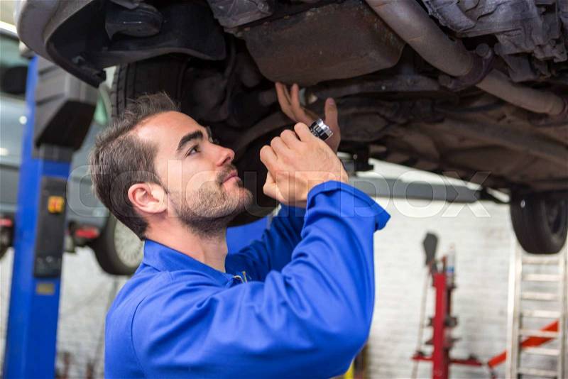 View of a Young attractive mechanic working on a car at the garage, stock photo