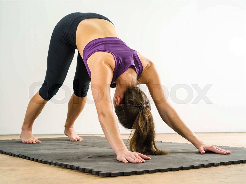 Photo of a healthy young woman doing the downward dog yoga position on a black floor mat, stock photo