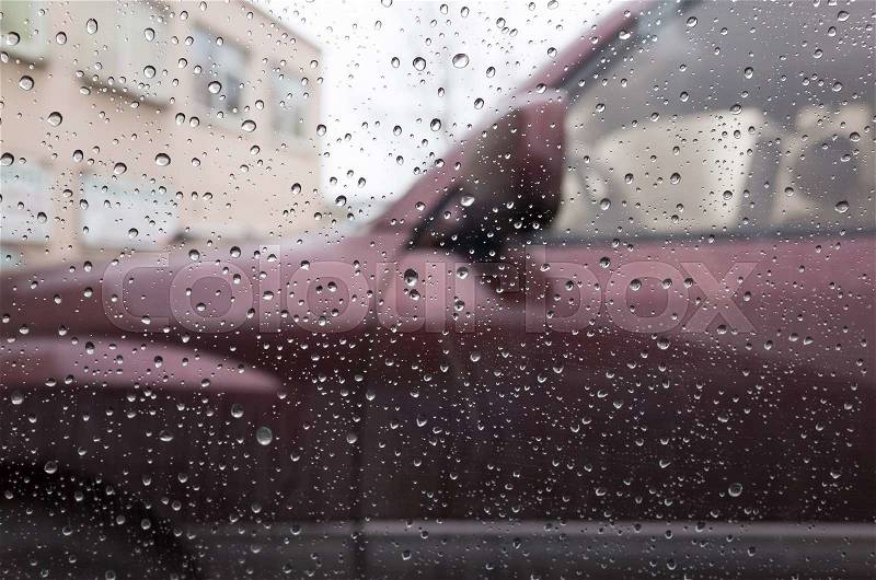 Wet car window with raindrops and a blurred car behind. Closeup photo with selective focus and shallow DOF, stock photo