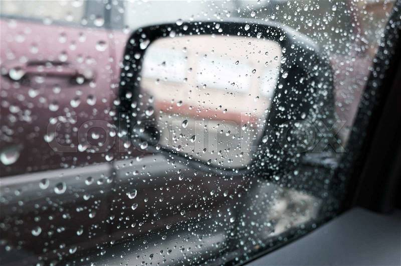 Wet car window with raindrops and a mirror behind. Closeup photo with selective focus and shallow DOF, stock photo