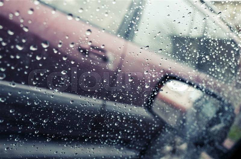Wet car window with raindrops and a mirror behind. Close-up photo with selective focus and shallow DOF, vintage tonal correction photo filter effect, stock photo