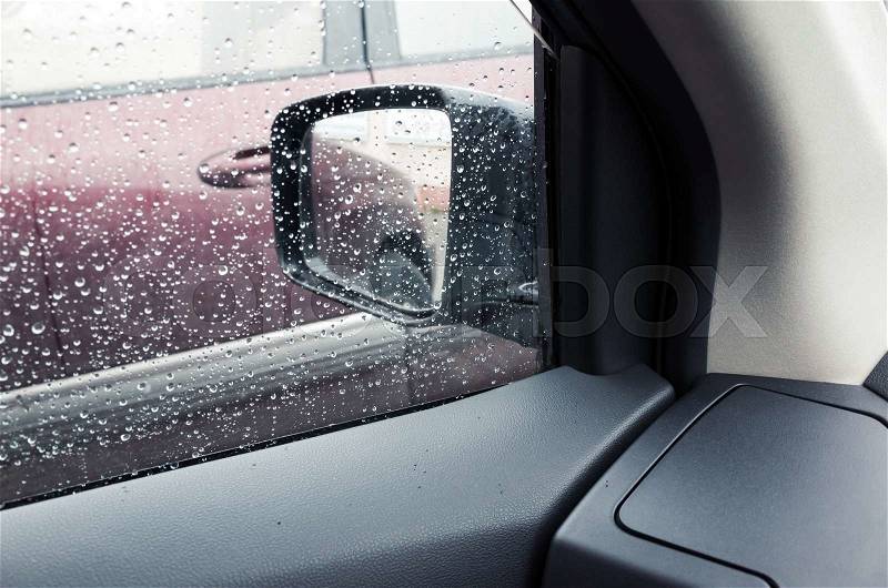 Wet car window with raindrops and a mirror behind. Close-up photo with selective focus and shallow DOF, stock photo