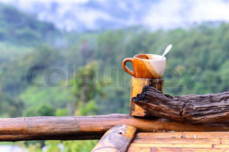 Coffee cup on bamboo coaster and wooden balcony with mountain view on the morning, stock photo