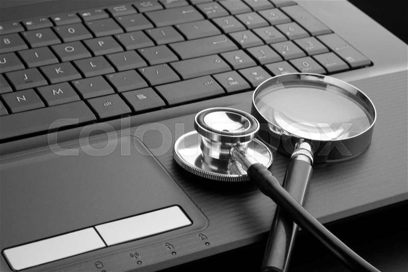 Medical stethoscope and magnifying glass on laptop keyboard. In B/W, stock photo