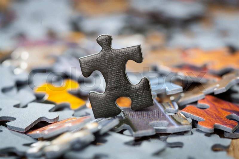 Black jigsaw puzzle piece on heap of color puzzle pieces. Shallow depth of field, stock photo