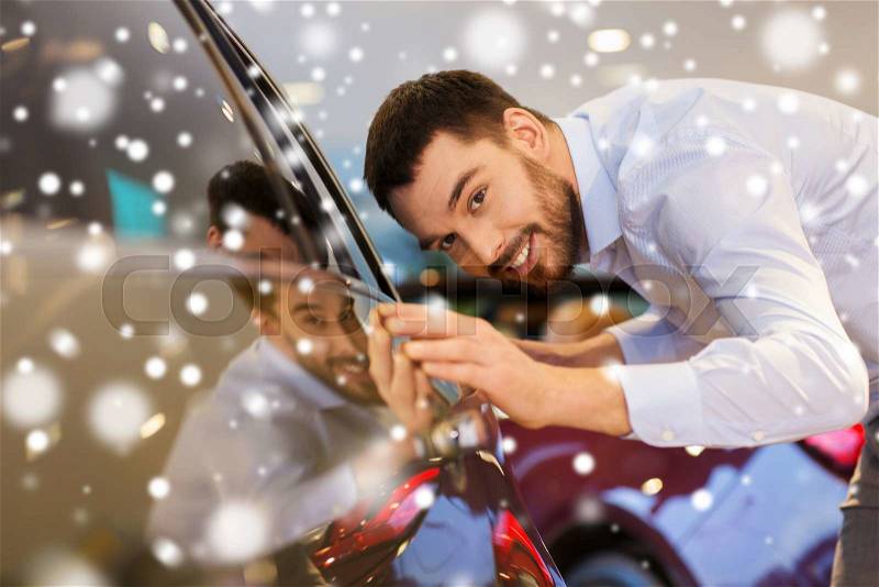 Auto business, car sale, consumerism and people concept - happy man touching car in auto show or salon over snow effect, stock photo